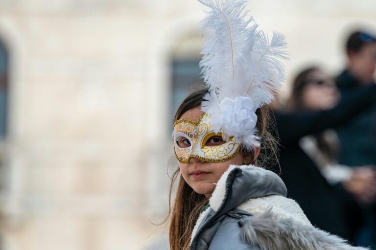A child wearing a decorative gold and white mask with feathers at a festival.