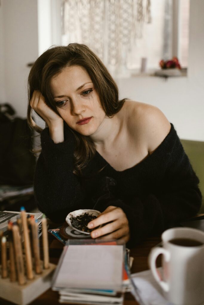A thoughtful woman sits indoors, holding a cup of coffee, reflecting.